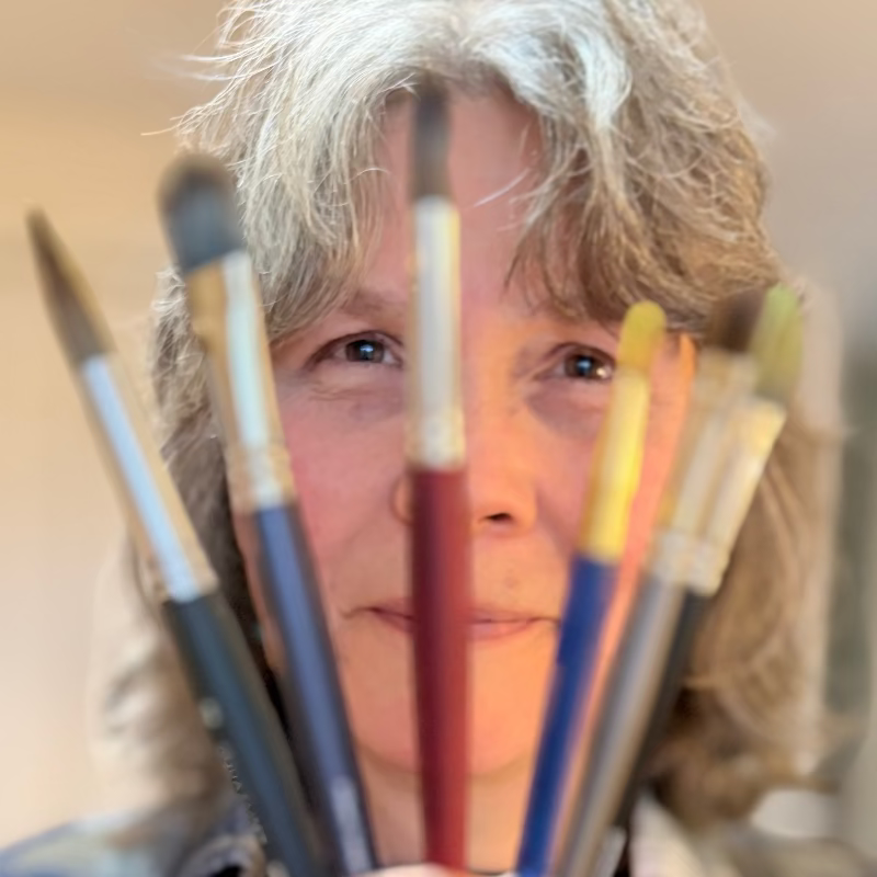 Person holding paintbrushes in front of their face with a blurred background