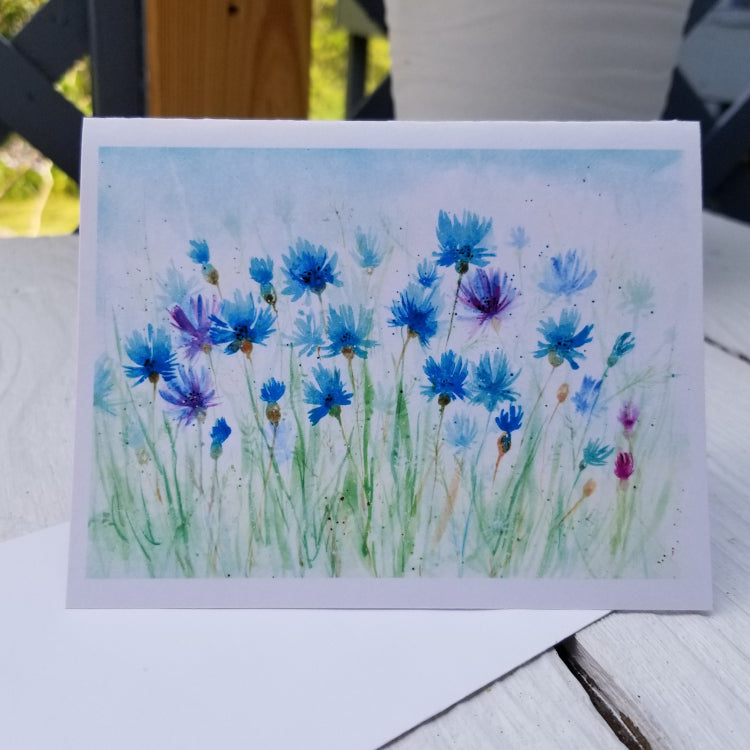 Card with watercolor design of blue and purple flowers on a wooden surface