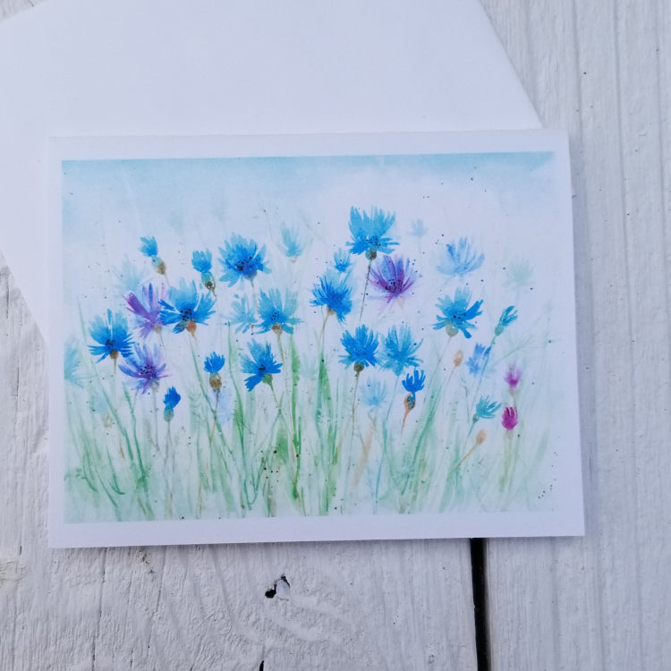Greeting card with watercolor design of blue and purple flowers on a light blue background