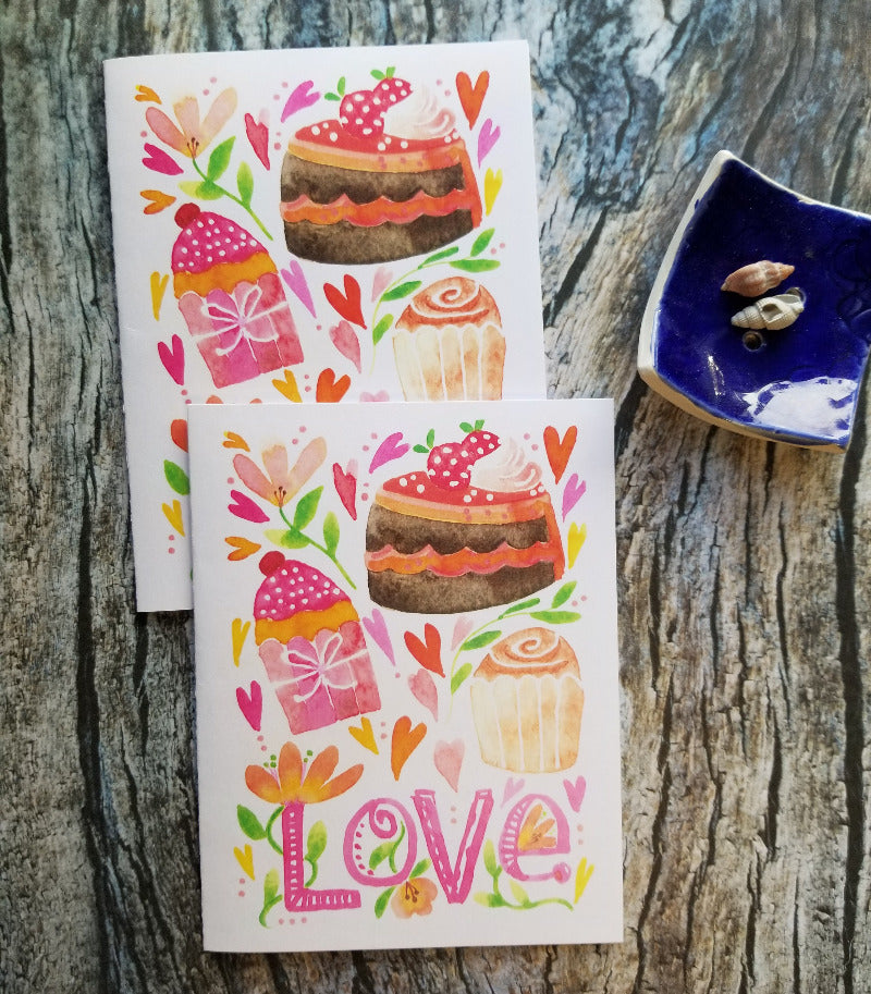 Two colorful Valentine greeting cards with cake illustrations on a wooden surface