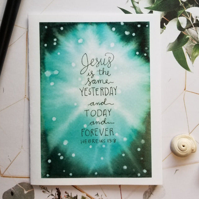 Framed artwork with 'Jesus is the same yesterday and today and forever' quote on a decorative surface with greenery.