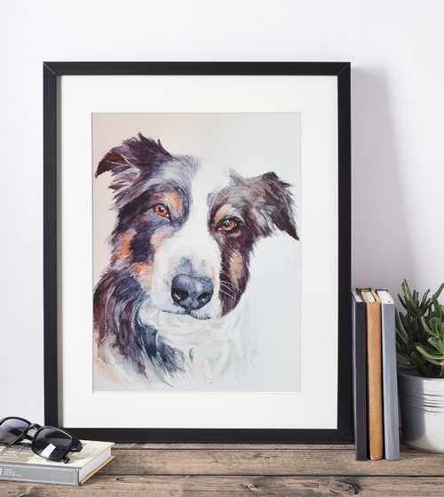 Framed artwork of a dog's face on a wall with books and a plant below.