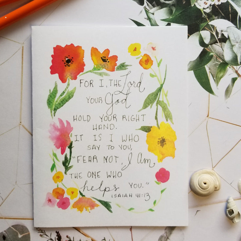 Floral card with Bible verse surrounded by stationery items on a geometric-patterned surface