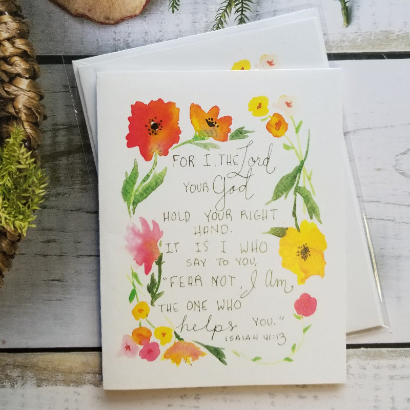 Greeting card with floral design and Bible verse on a wooden surface with natural elements.