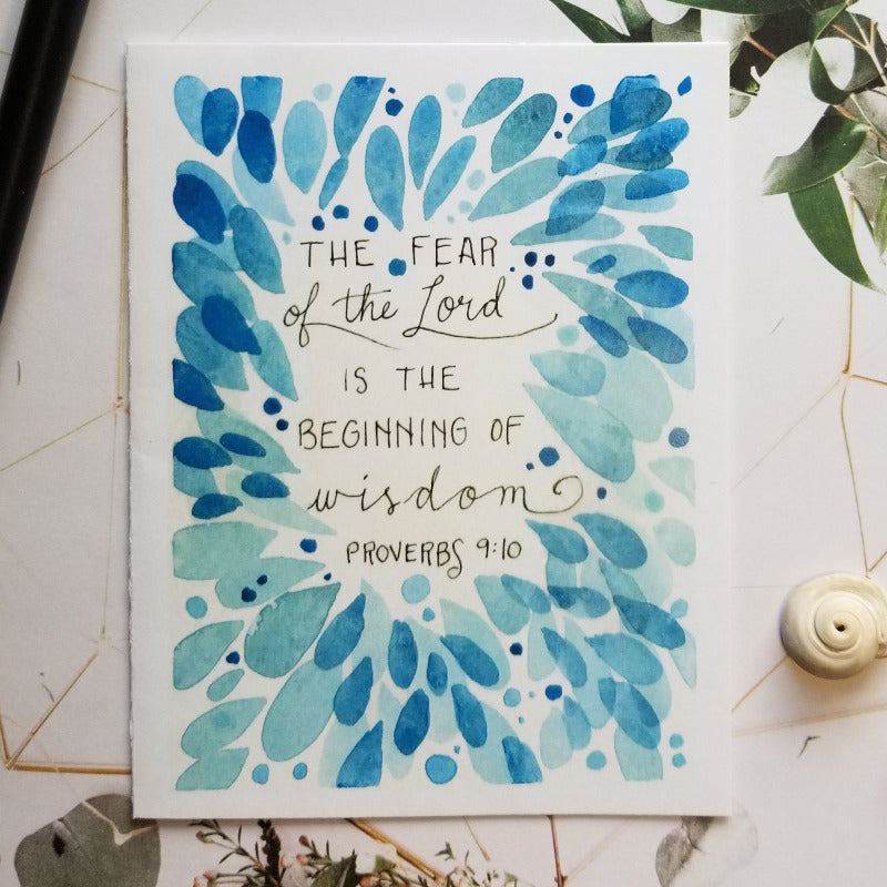 Card with blue leaf design and Proverbs 9:10 text on a white background with greenery.