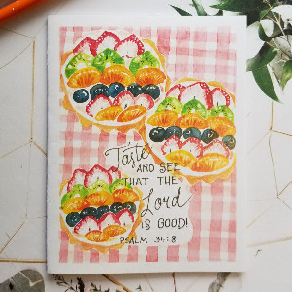 Notebook with fruit illustration and text on a decorative surface with greenery