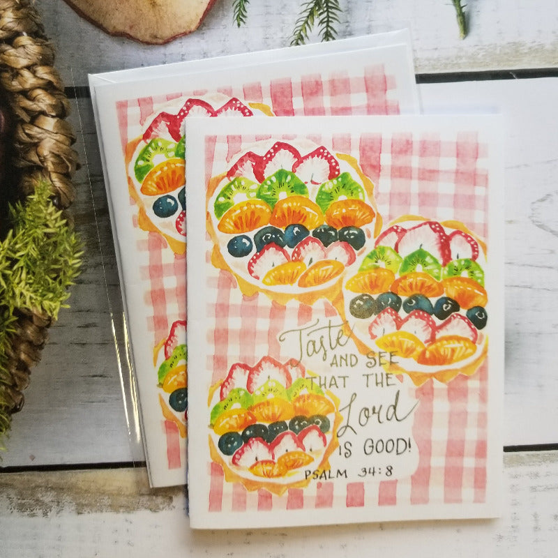 Two greeting cards with fruit illustrations and bible verse on a checkered background, surrounded by decorative elements.